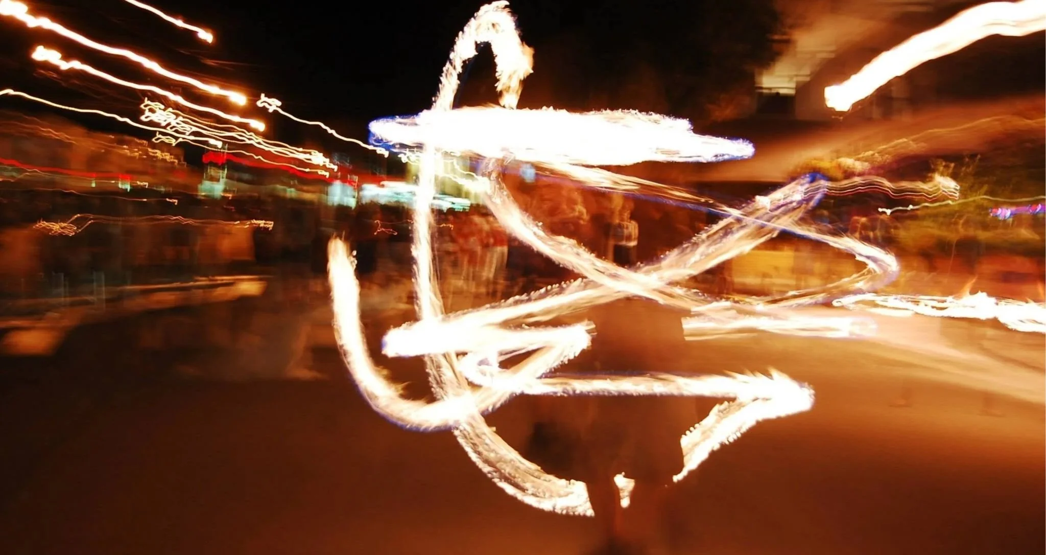Light trails created by moving light sources at night, forming abstract patterns with bright white and warm orange colors.