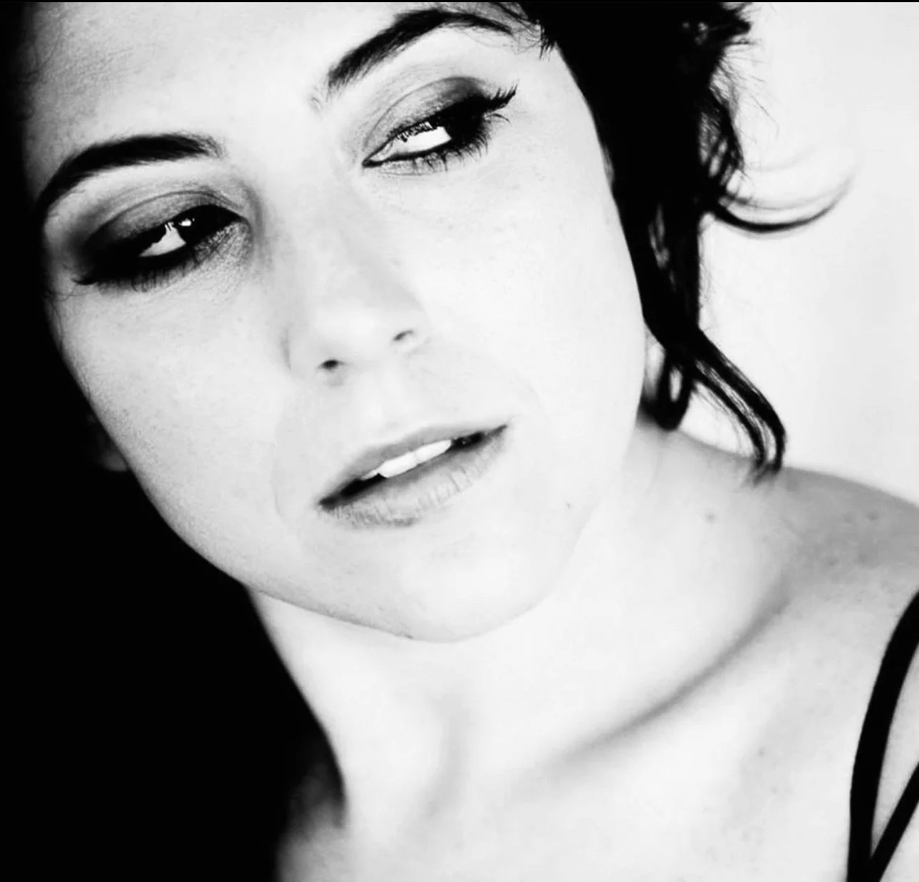 Black and white close-up photograph of a woman's face with tousled dark curly hair, showing her eyes, nose, and lips in a relaxed expression.