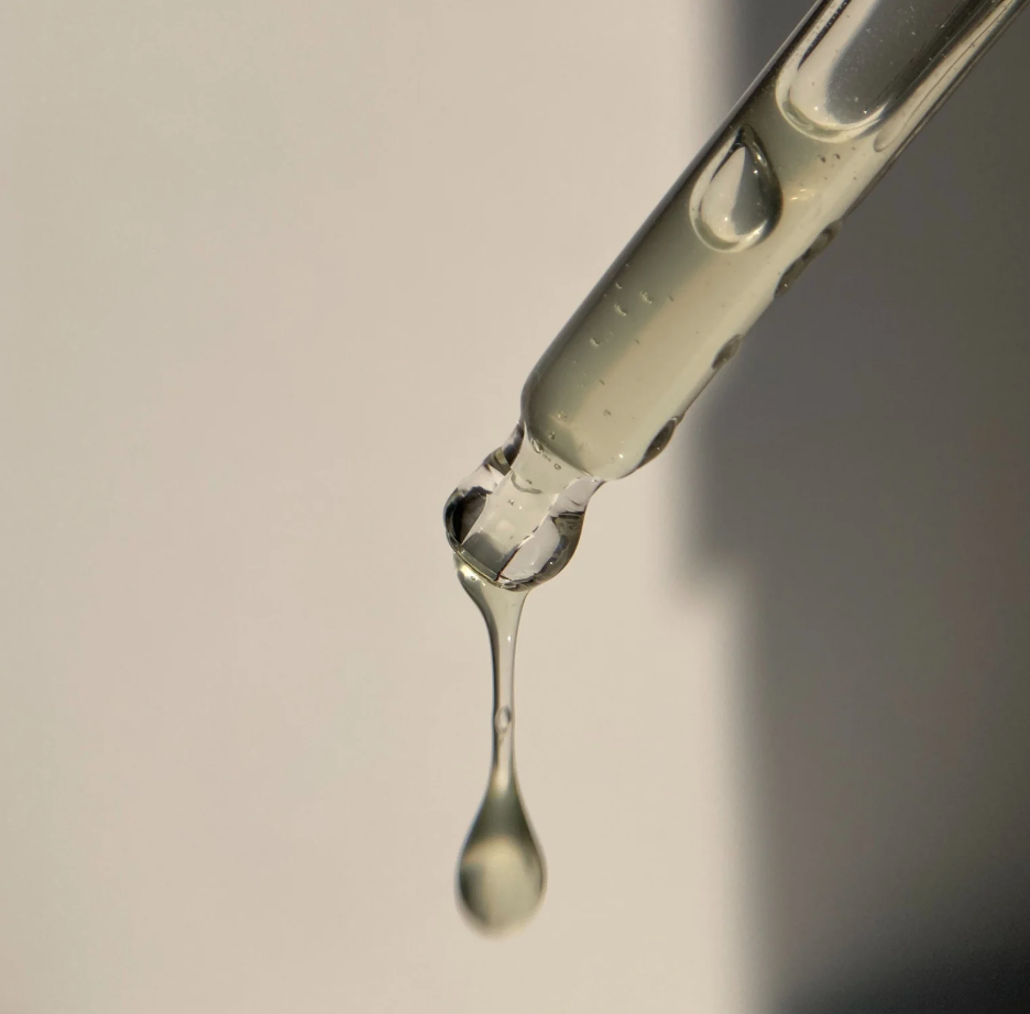Ampolla de pipeta con líquido transparente y gotas cayendo.