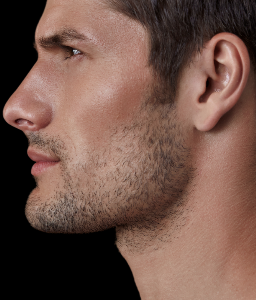 Perfil de un hombre joven con barba rala y piel clara, mirando hacia la izquierda, con fondo negro.