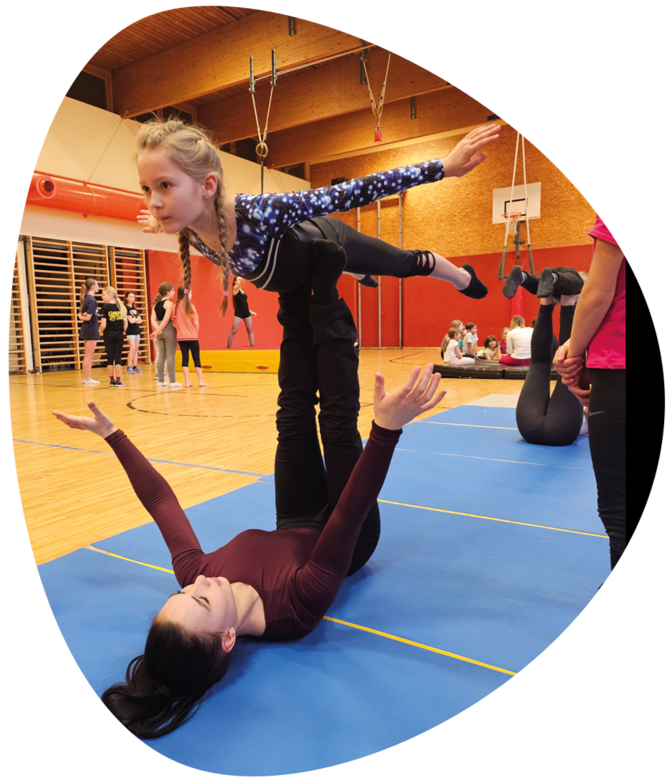 Open Circus School: Frau liegend balanciert Kind auf Fußsohlen