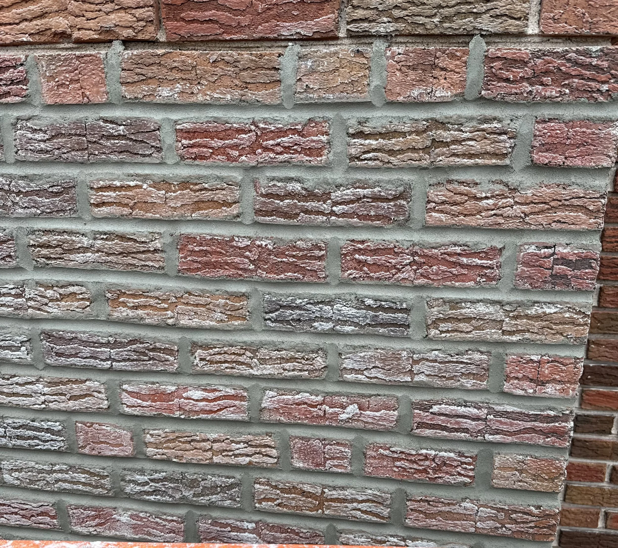 Close-up of a brick wall with red and brown bricks, gray mortar, and some white paint or residue on the bricks.