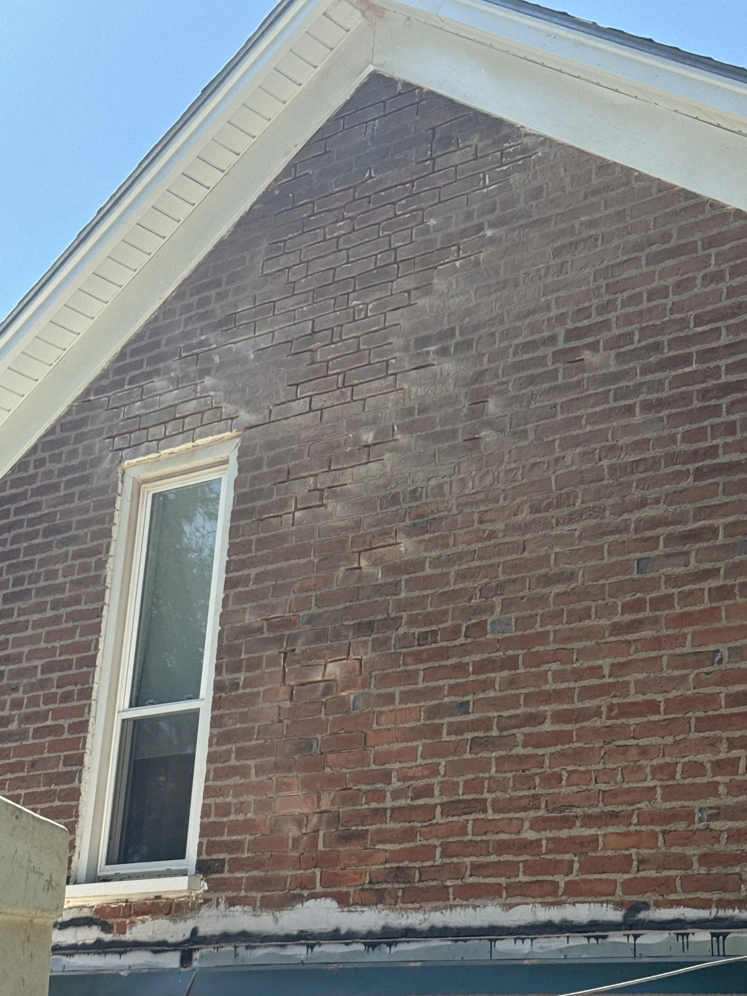 Close-up of a brick exterior wall of a house with a window, partially under construction or renovation, with visible mortar and construction materials at the bottom.