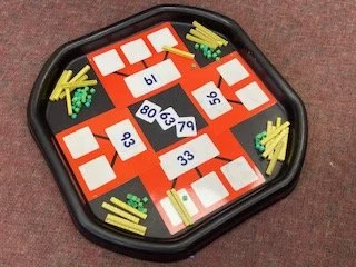 A board game with numbered tiles, some blank tiles, and colored plastic sticks in the corners on a red surface.