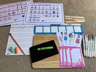 School supplies including flashcards, alphabet chart, writing worksheet, pencil with eraser, sticky notes, a black card, colorful markers, and decorated cards with illustrations of children.