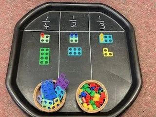Educational tabletop game with three sections labeled 1/4, 1/2, 1/3, each containing matching colored number cubes, with baskets of additional cubes in front.