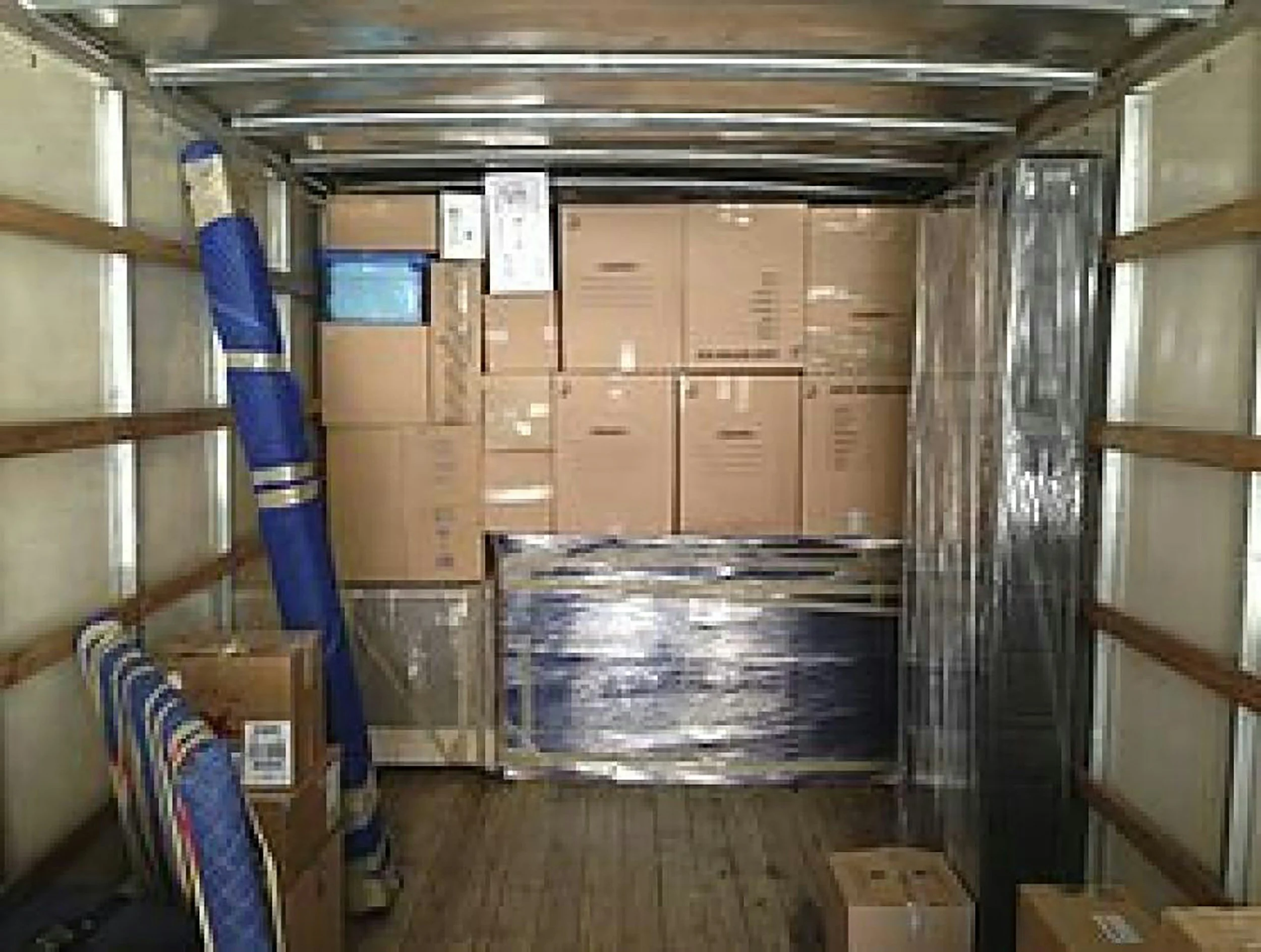 A storage room with metal framing shelves, some shelves wrapped in blue and striped fabric, and boxes stacked against the back wall.