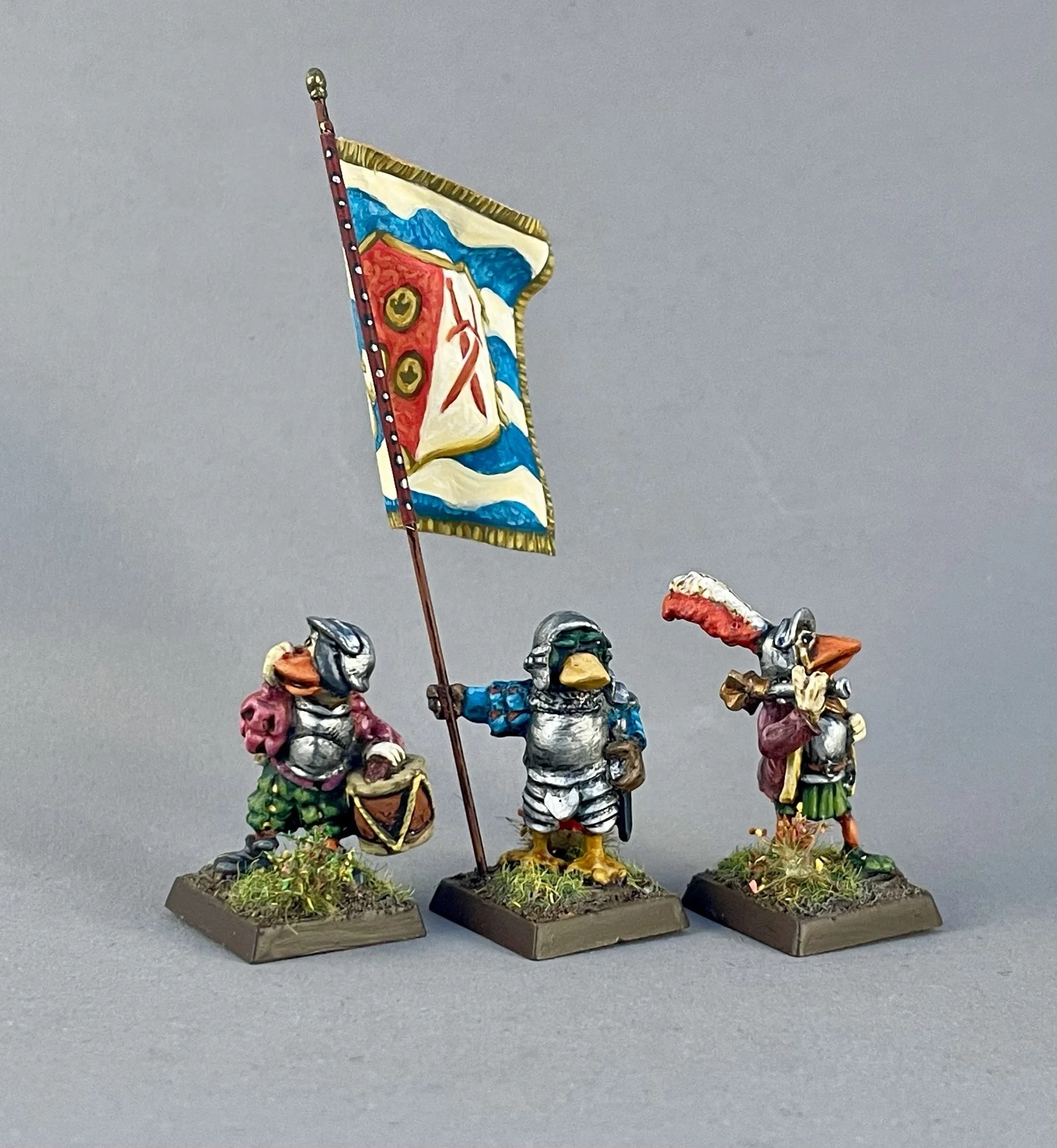 Miniature figurines of soldiers holding a colorful flag with a mountain scene, standing on bases with grass and dirt details.