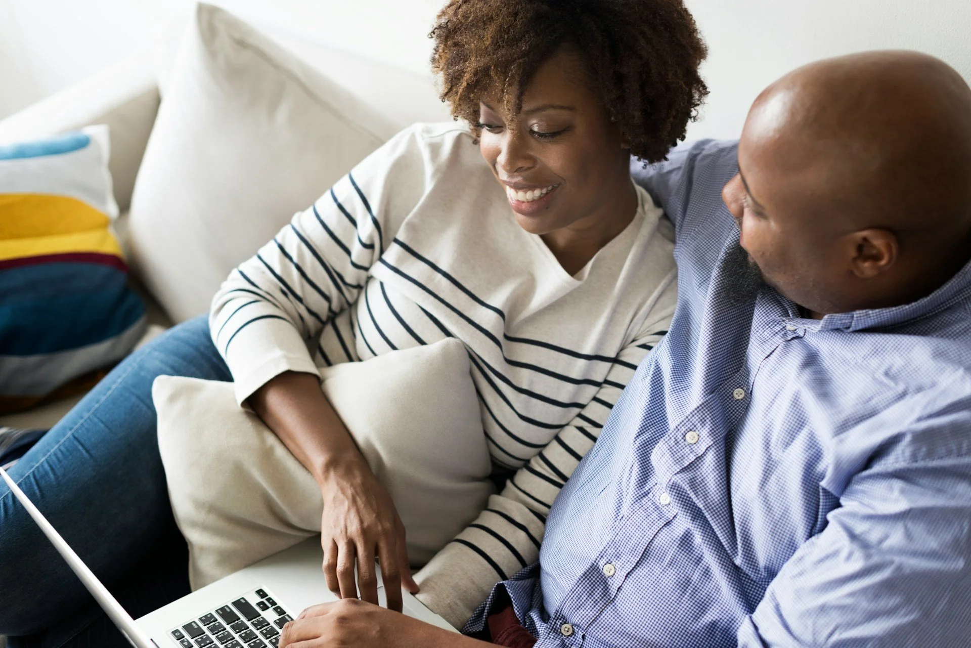 A woman and a man sitting closely together on a couch, looking at a laptop, with the woman smiling.