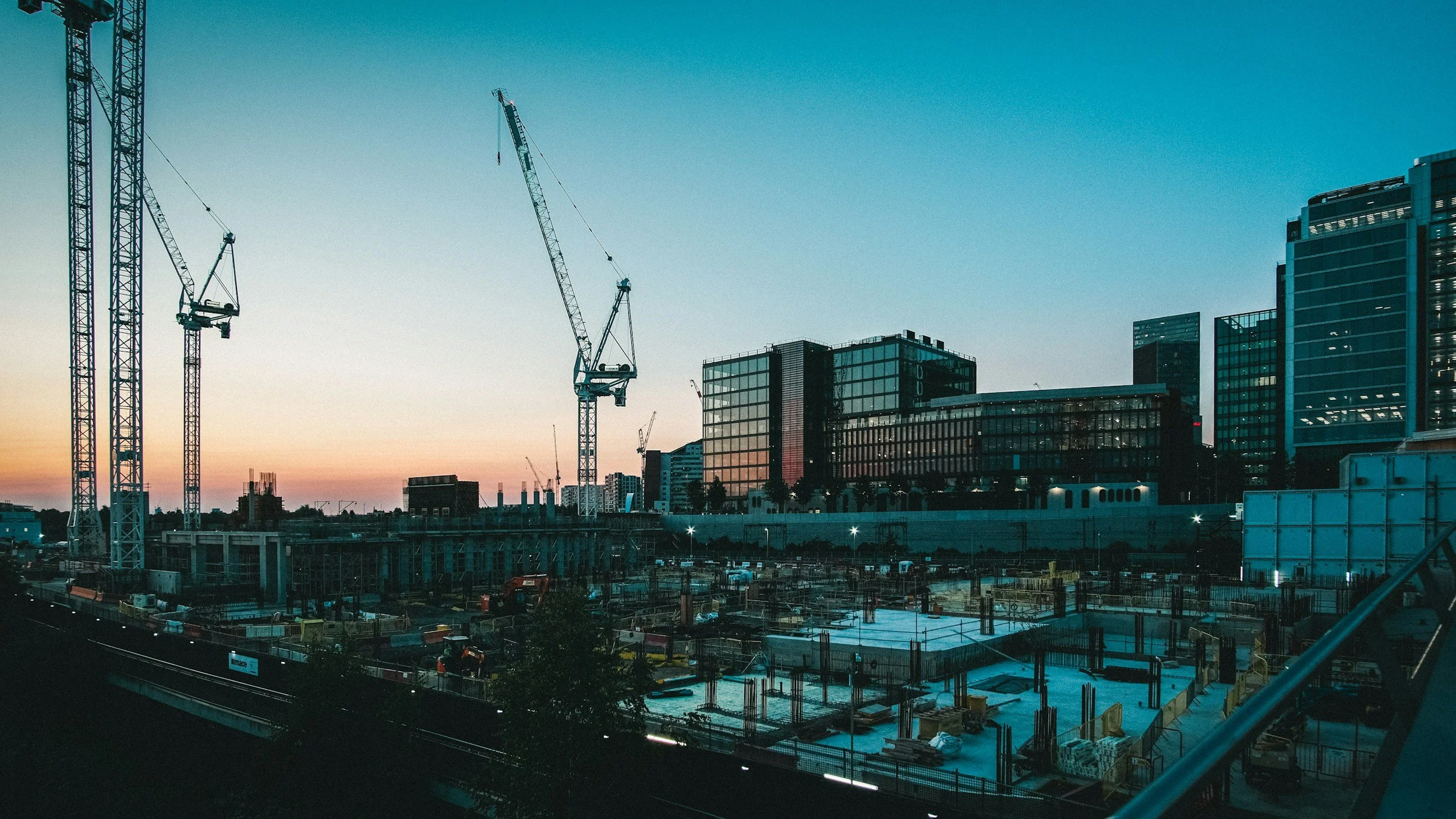 A cityscape during sunset with several construction cranes and modern high-rise buildings under construction.