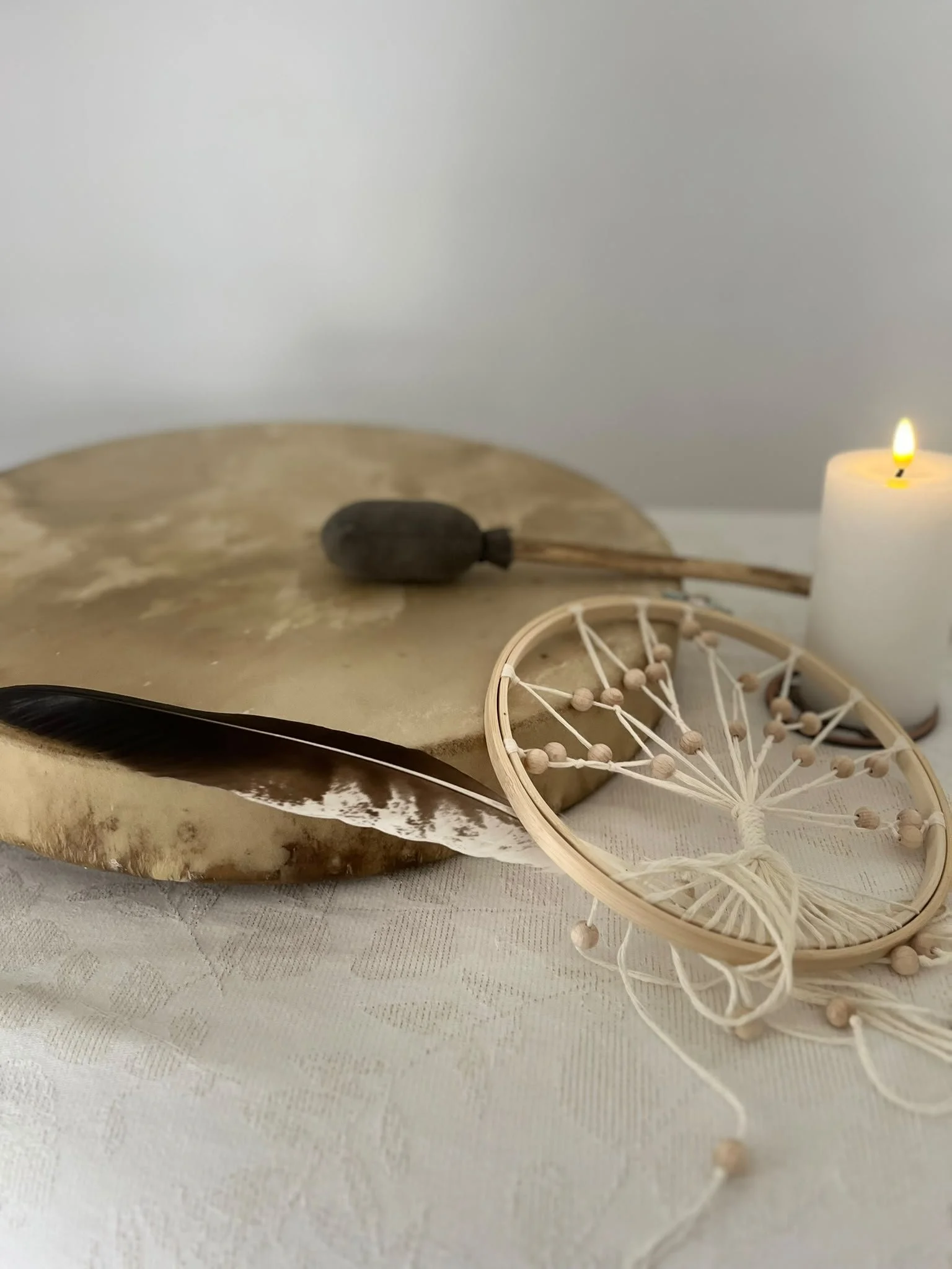 Une pierre de flint, une plume noire, une bougie allumée, un attrape-rêves en bois et des éléments en cordelettes sur une table en surface blanche.