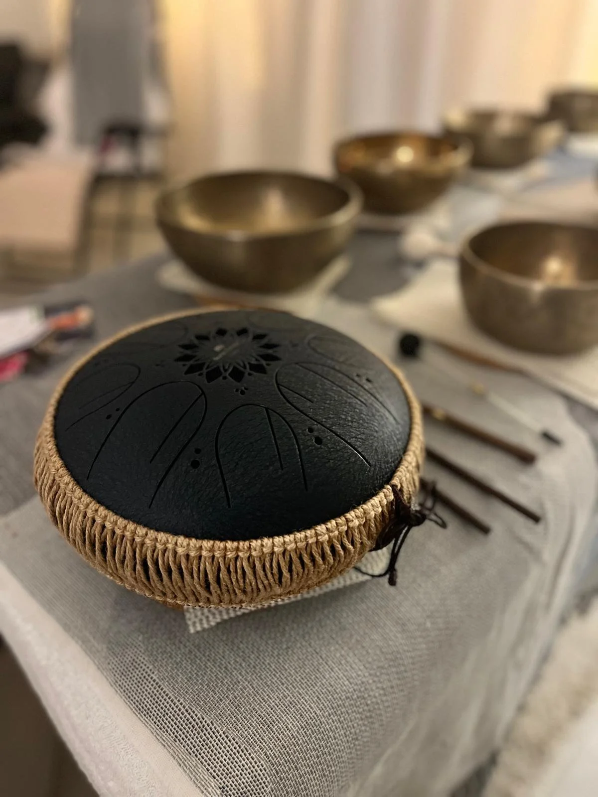Un instrument de musique en forme d'olive en cuir noir, entouré d'une cordelette beige, posé sur une table avec d'autres instruments métalliques flous à l'arrière.