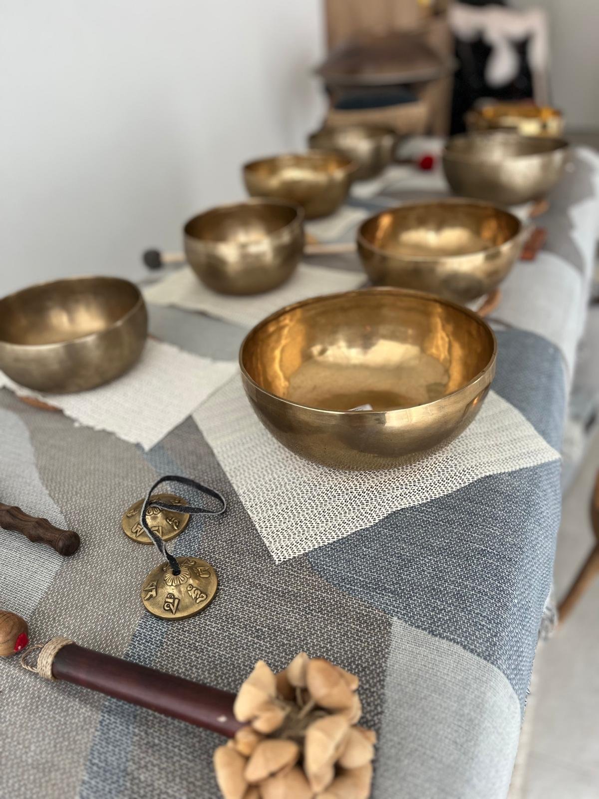 Une rangée de bols en métal doré sur une nappe blanche, avec divers objets liés à la musique ou à la décoration en premier plan.