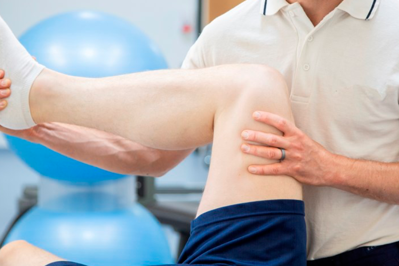 Physical therapist holding a patient's leg during rehabilitation therapy in a clinic.