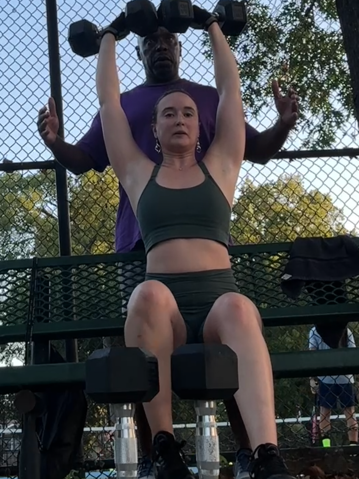 Sara performing a seated dumbbell shoulder press during outdoor strength training at Spotts Park in Houston.