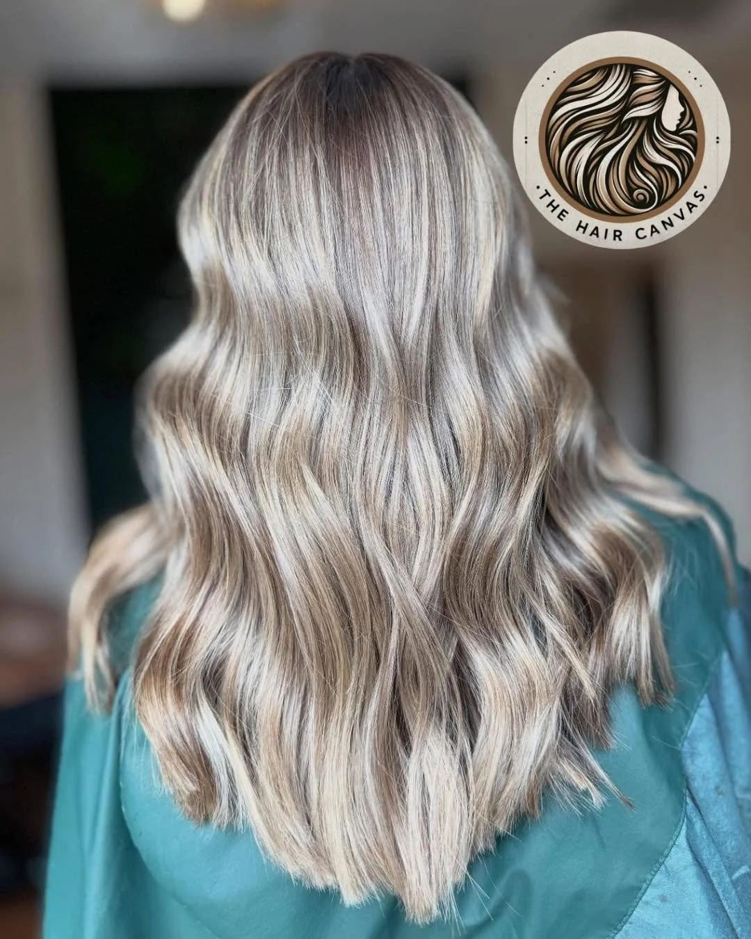 Back of a person's head with long, wavy blonde hair with darker roots, in a salon setting.