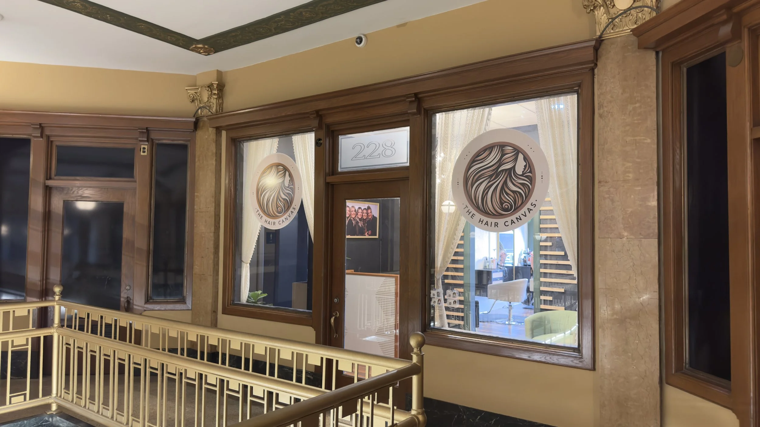 Interior view of a hair salon called 'The Hair Canvas' with large windows and curtains, decorated with ornate wood trim, gold accents, and a small framed photo on the wall