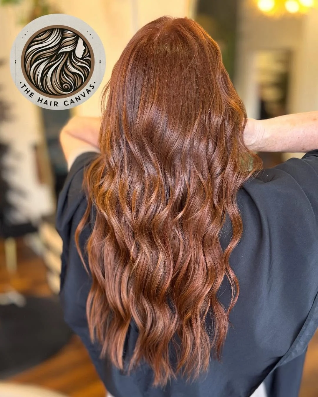 Back view of a woman with long, wavy, chestnut brown hair in a salon.
