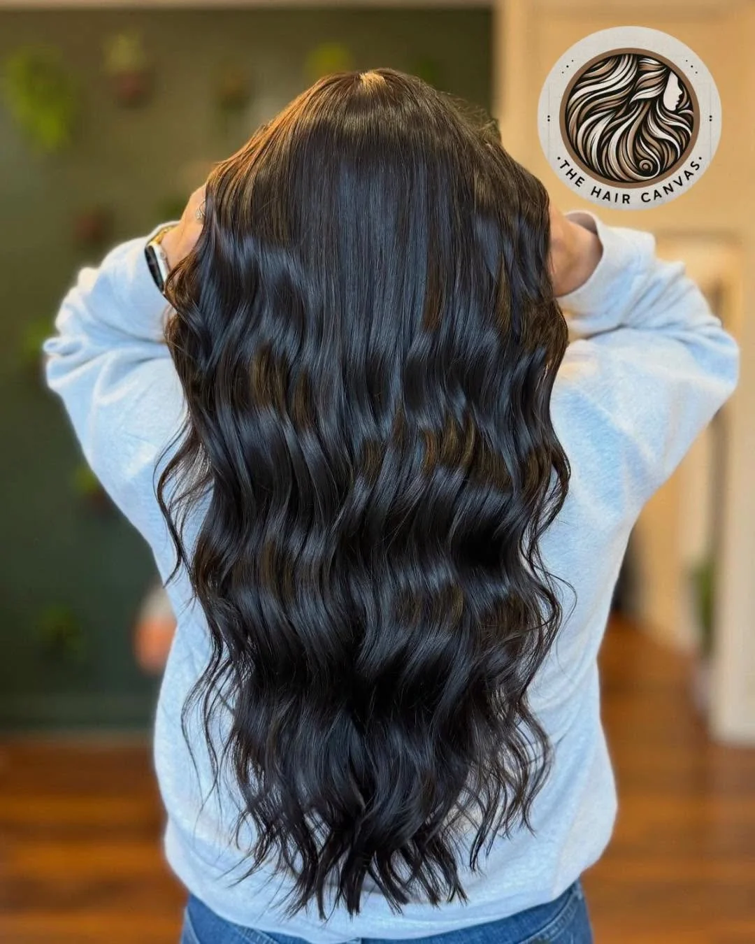Long, wavy, dark brown or black hair flowing down the back of a person wearing a light gray hoodie.