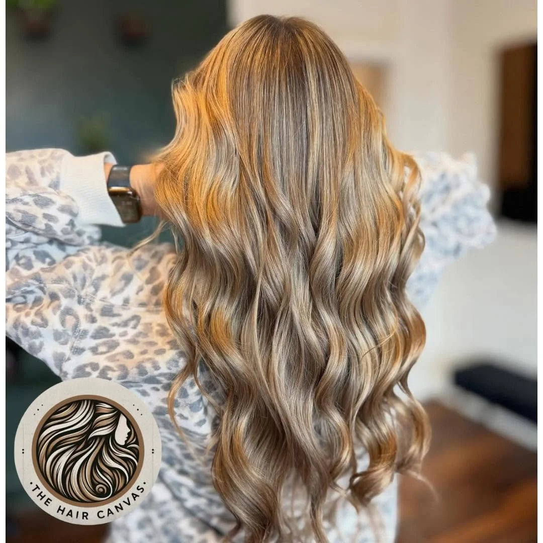 Long, wavy, blonde hair with highlights, worn by a person with their back to the camera. The person is wearing a leopard print top and is indoors.
