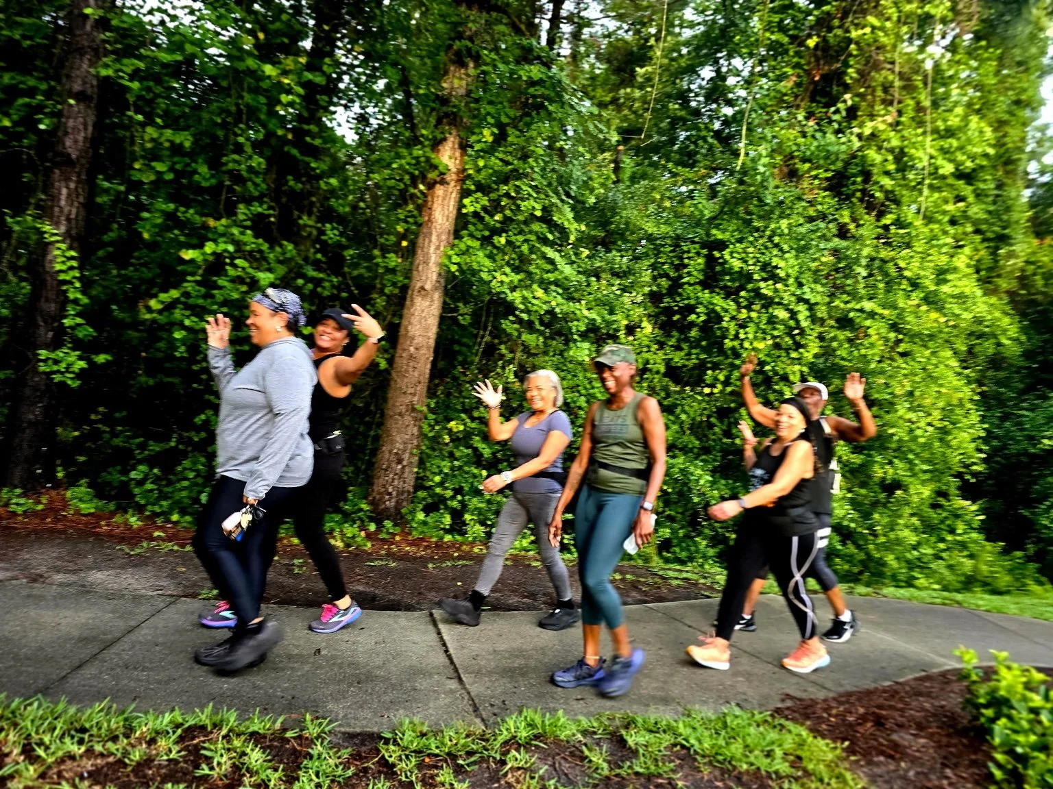 Group of six diverse women walking and smiling together outdoors during a TransformHer community wellness walk, encouraging movement, connection, and healthy living.