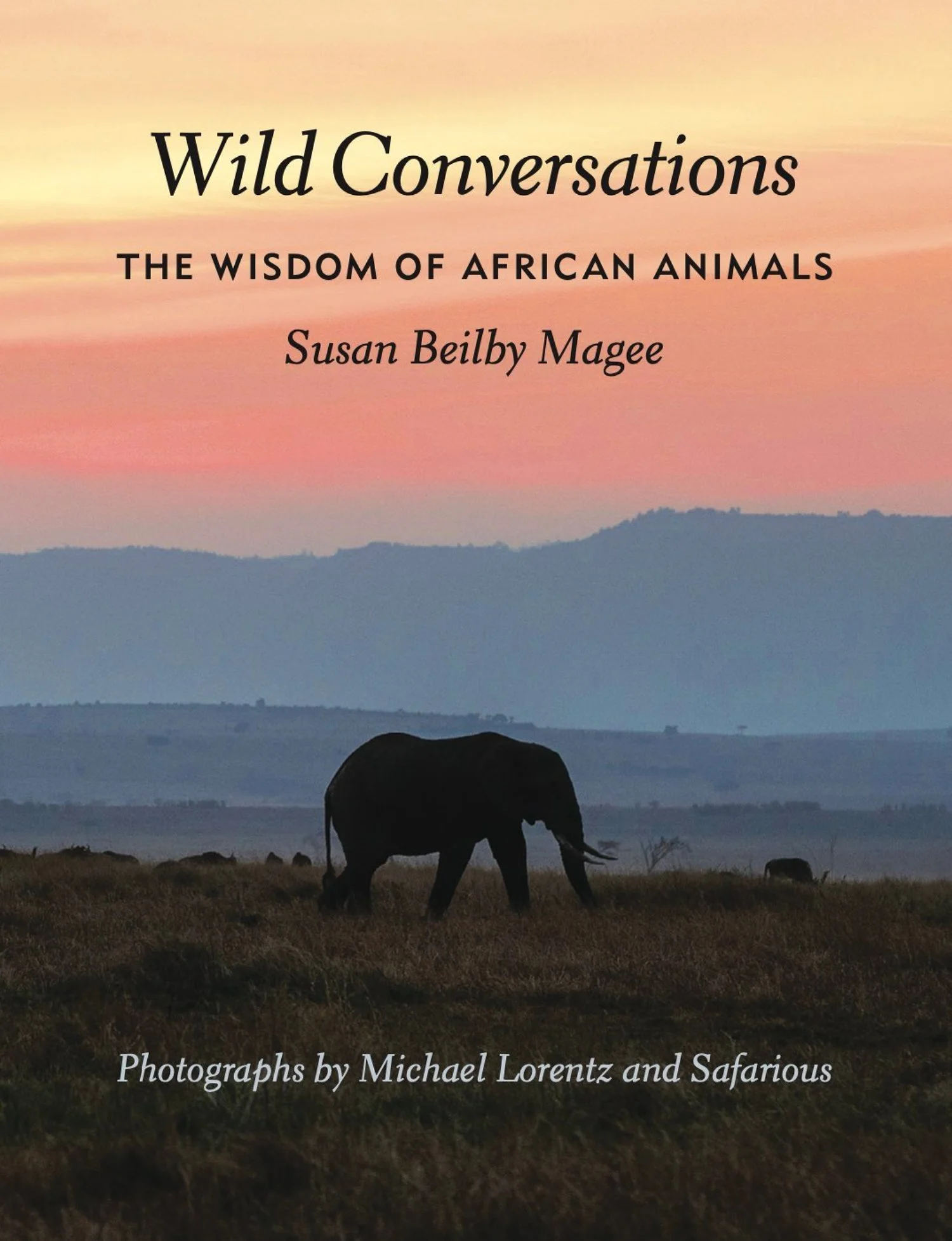 A silhouette of an elephant walking in the grasslands during sunset or sunrise, with layered mountains in the background and a pink and orange sky on the cover of Wild Conversations.