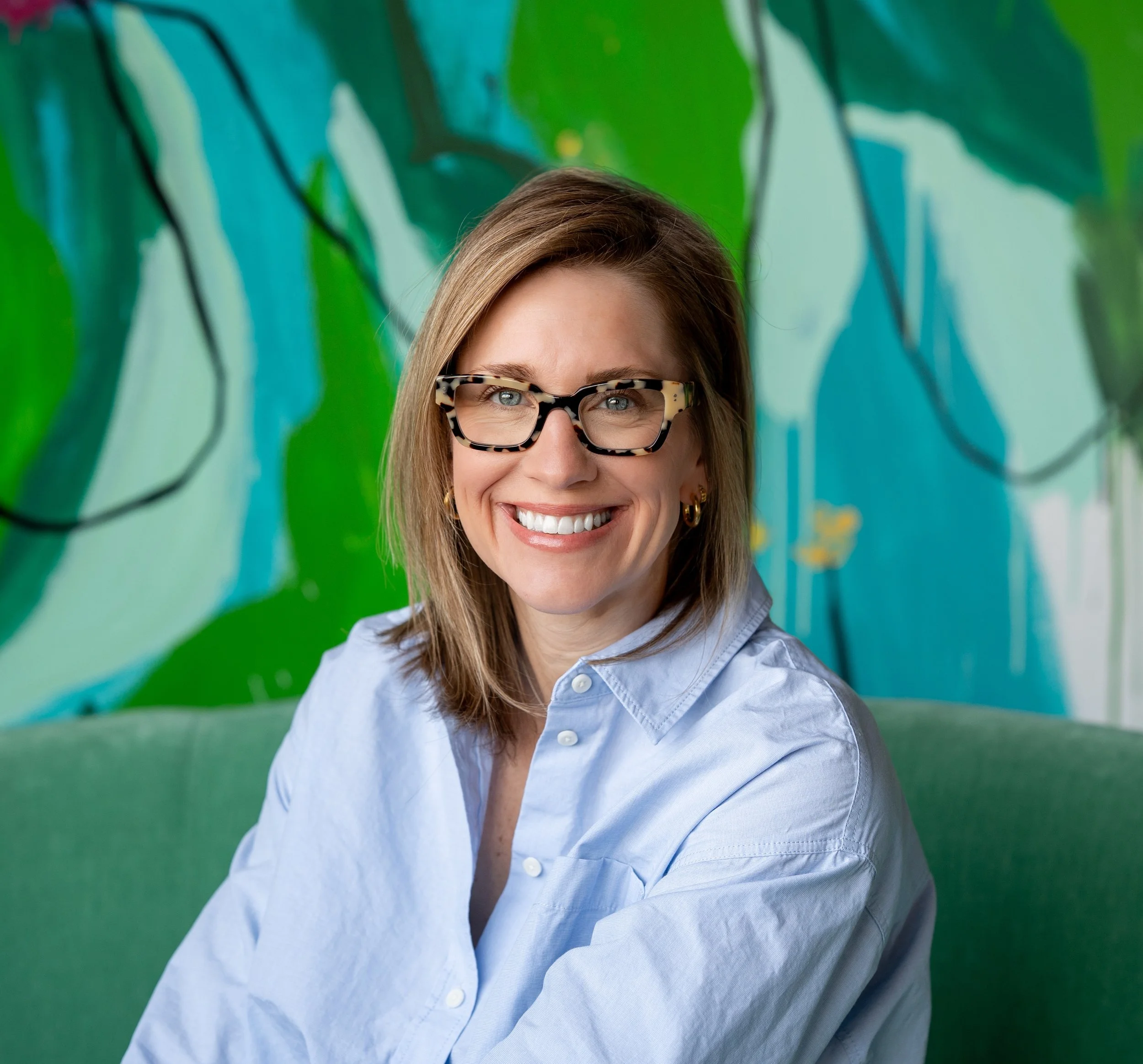Emily Dingmann (blonde hair and glasses smiling in front of a colorful abstract mural background), a food brand marketing consultant.