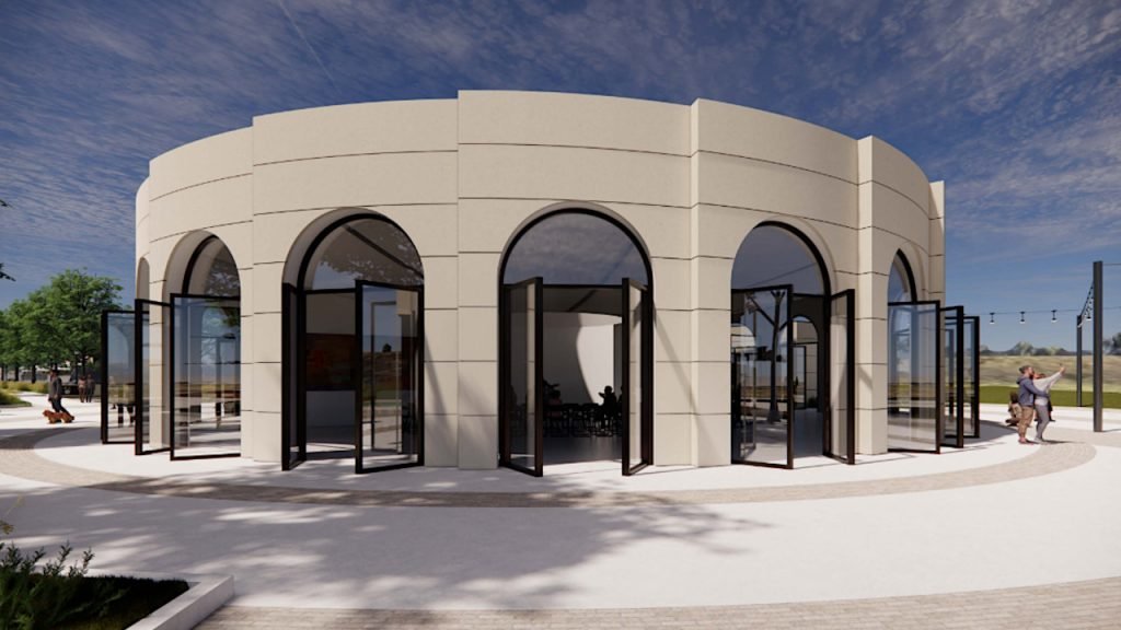 A modern round building with large arched windows and glass doors, located in a park-like setting with trees and open space.