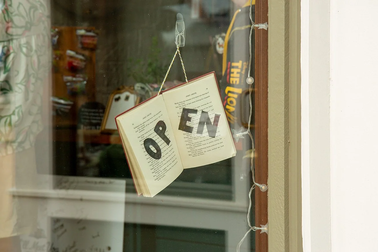 Open book hanging in a window with the words "OPEN" spelled out with large black letters.