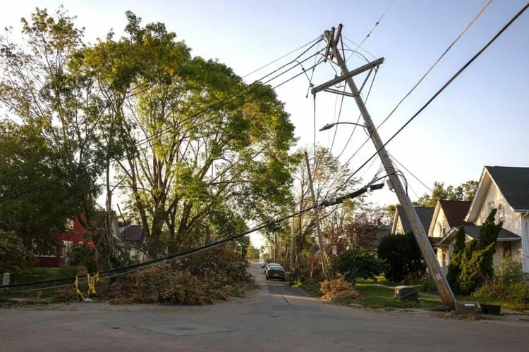 A fallen tree and a utility pole blocking a residential street after a storm.