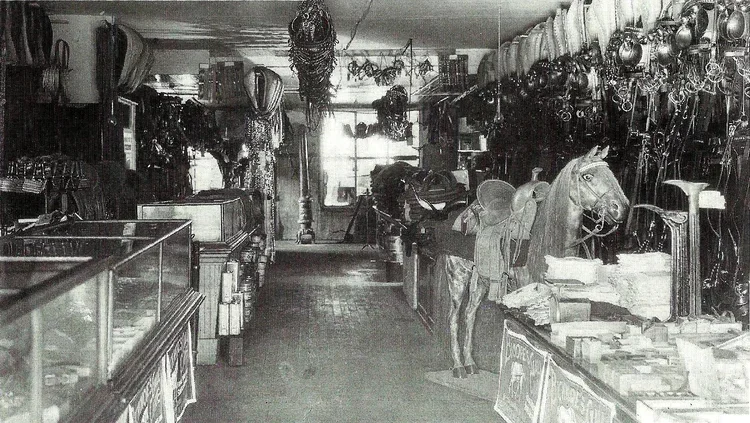 Inside a vintage shop with shelves and displays of various items, including a horse mannequin, lamps, hats, and other accessories, arranged along the walls and counters.