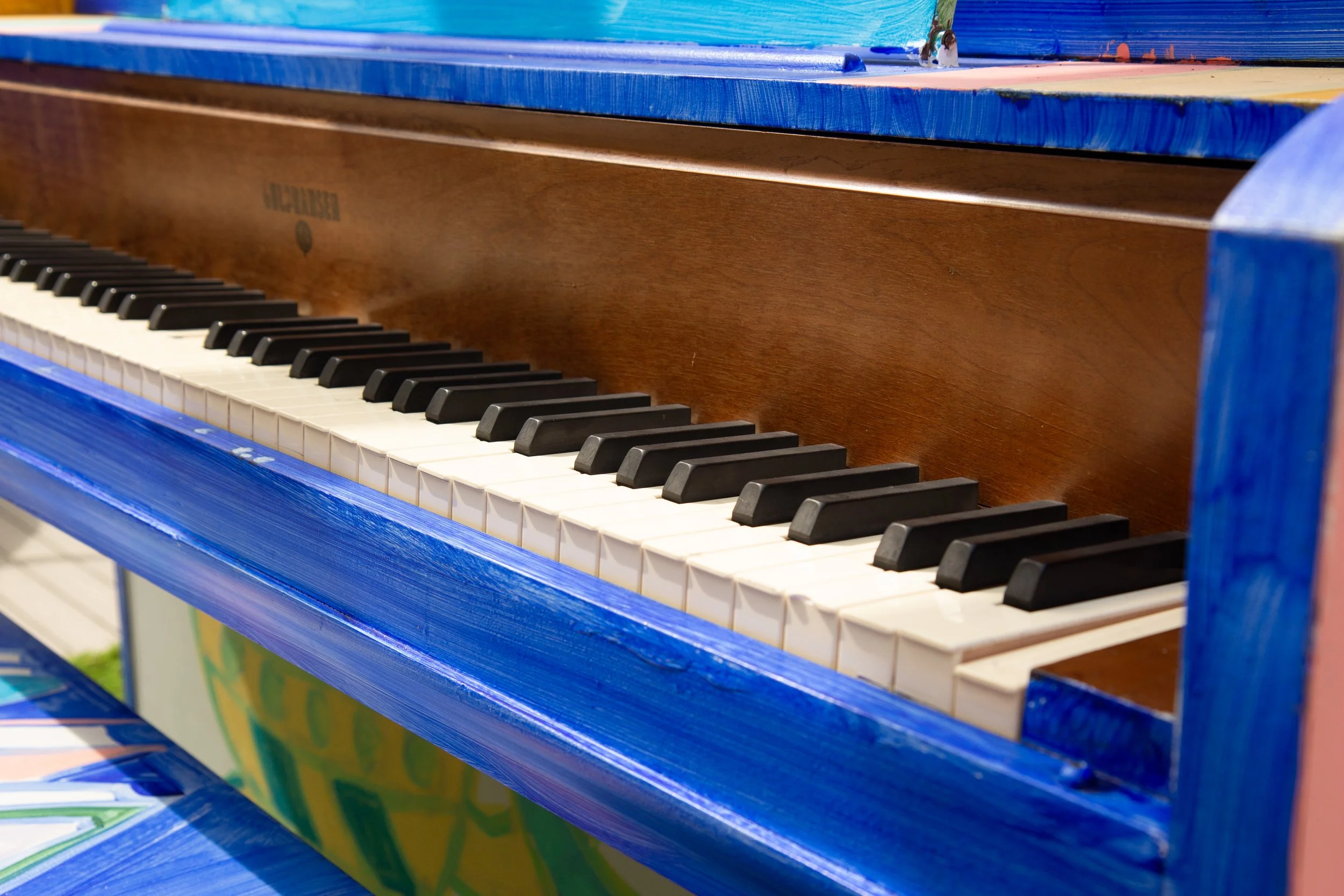 Close-up of a colorful painted wooden piano, showing black and white keys with blue sides and a brown wood front.