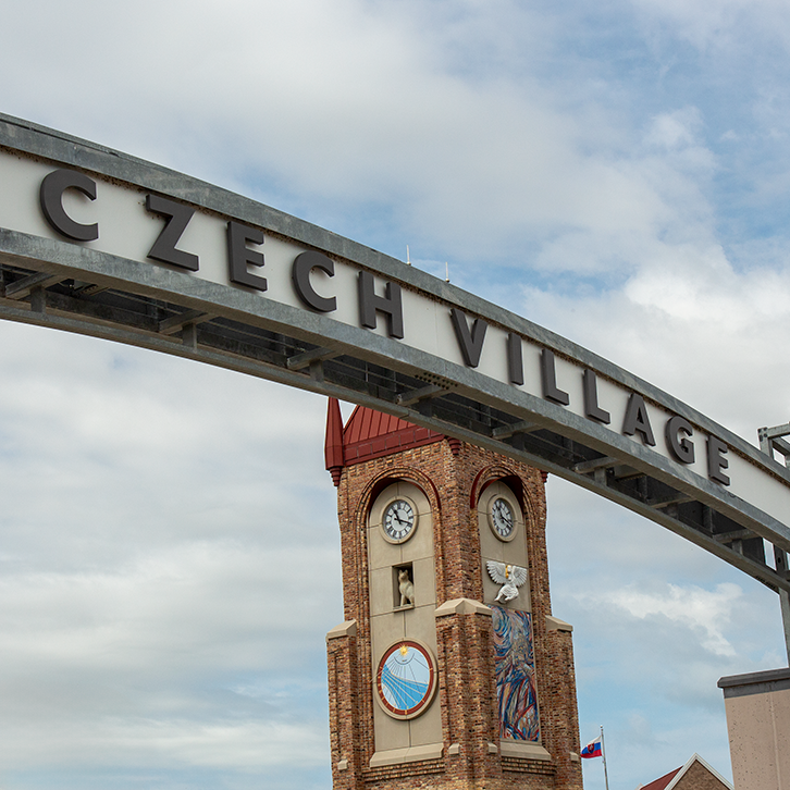 A clock tower and a sign that reads 'Czech Village' under a partly cloudy sky.