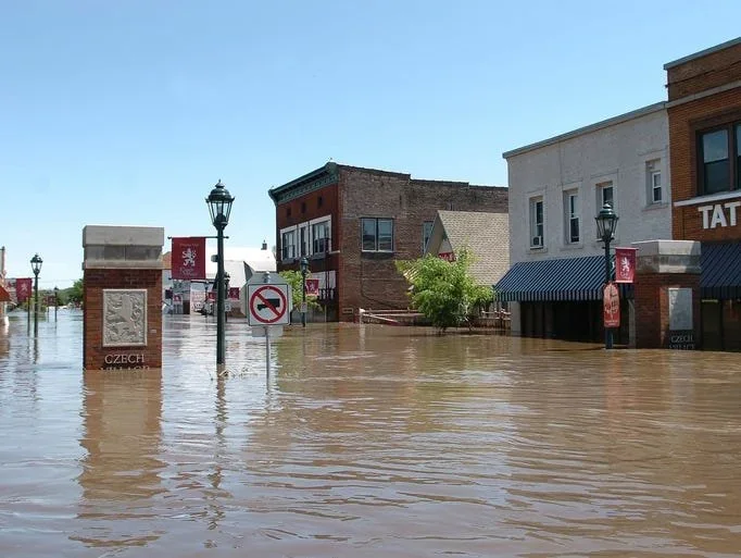 Flooded street in a small town with water reaching the buildings' front doors, street lamps, and signage for Czech culture.