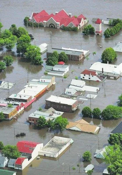 Aerial view of a flooded neighborhood with water covering streets and some buildings, and a church with a red roof in the background.