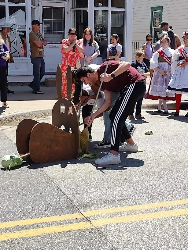 People gathered around cleaning up a street, some wearing traditional dresses, during a community event.