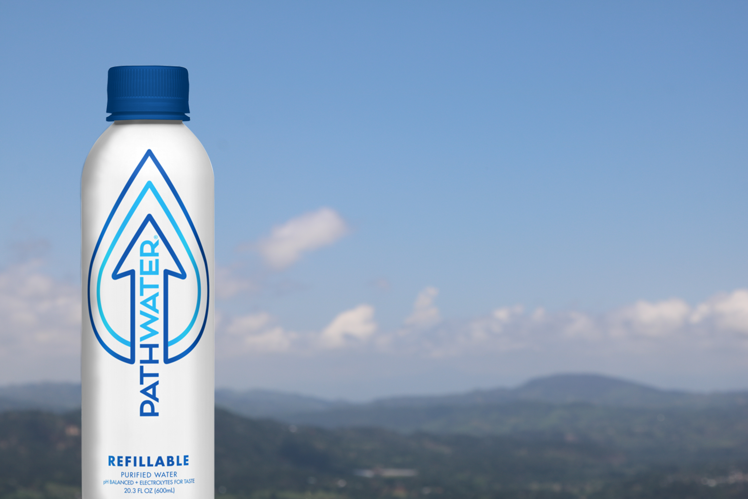A white plastic bottle with a blue screw cap, labeled with blue and black text, stands against a blue sky background with scattered clouds. The label indicates it is a refillable bottle of purified water.