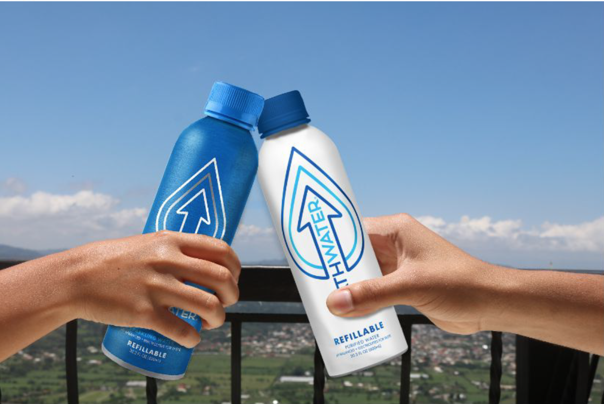 Two hands holding bottles of water, one blue and one white, with a mountain and sky background.