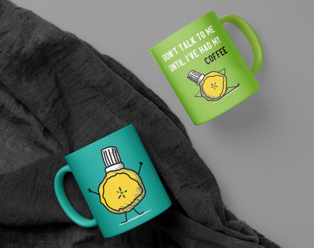 Two colorful coffee mugs with cartoon lemon characters, one green with the text "Don't talk to me until I've had my coffee," and one blue with a lemon character, resting on a dark gray fabric surface.