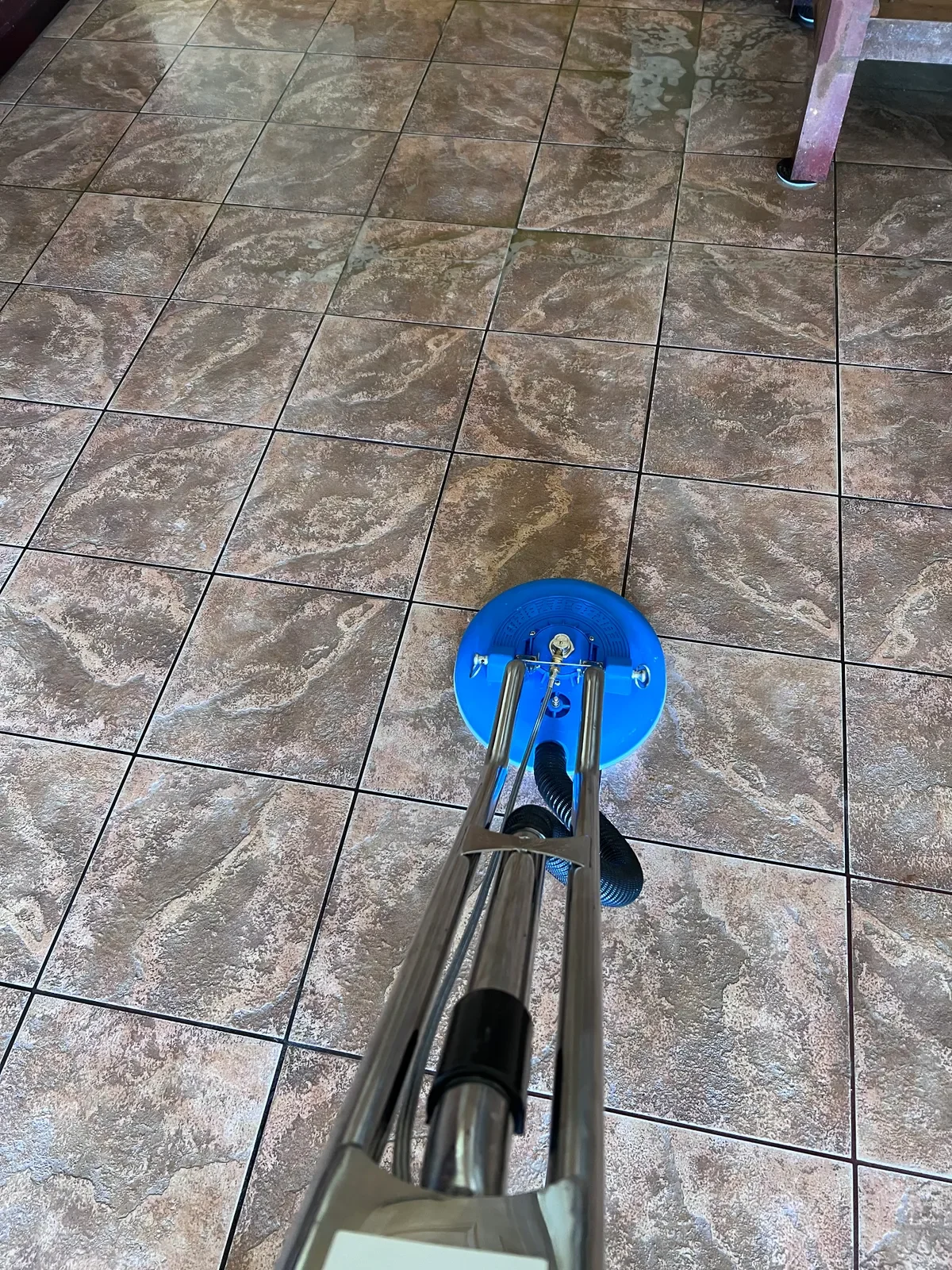 A floor with dirty white tiles and a floor cleaning mop with a yellow scrubber head.