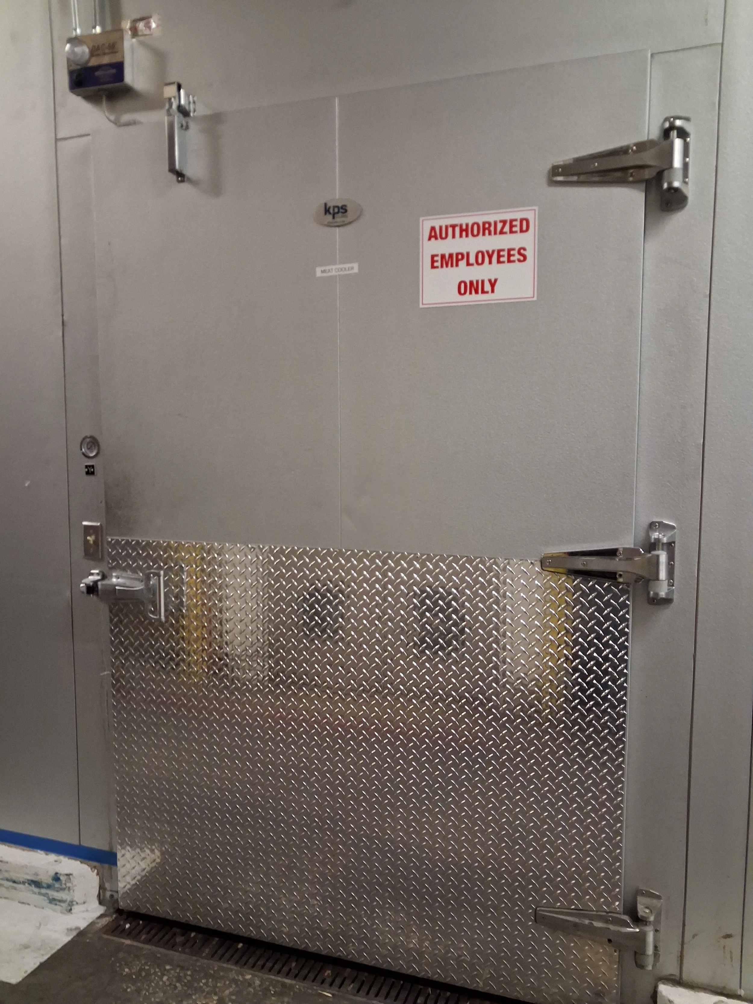 A metallic door with a diamond plate pattern, equipped with a latch and hinges, and a red and white 'Authorized Employees Only' sign on it.