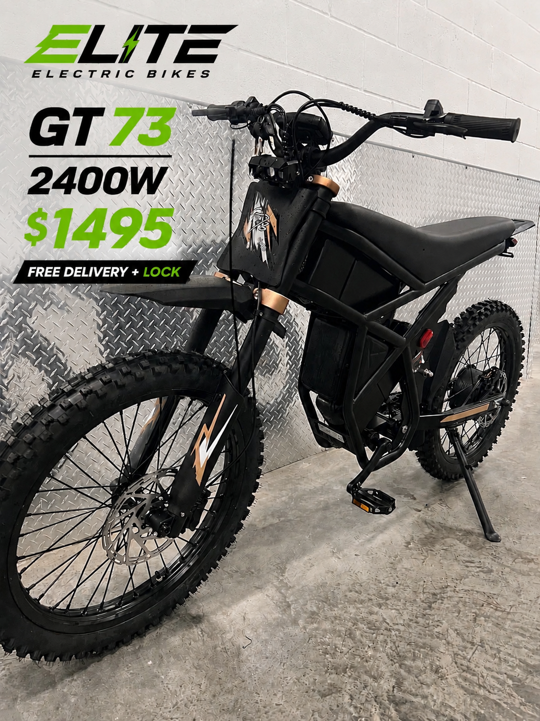 An electric mountain bike with black frame and fat tires, positioned indoors against a wall with industrial flooring and diamond plate wall panel. Promotional text on the wall advertises the bike model GT 73, 2400W power, priced at $1495, with free delivery and lock.