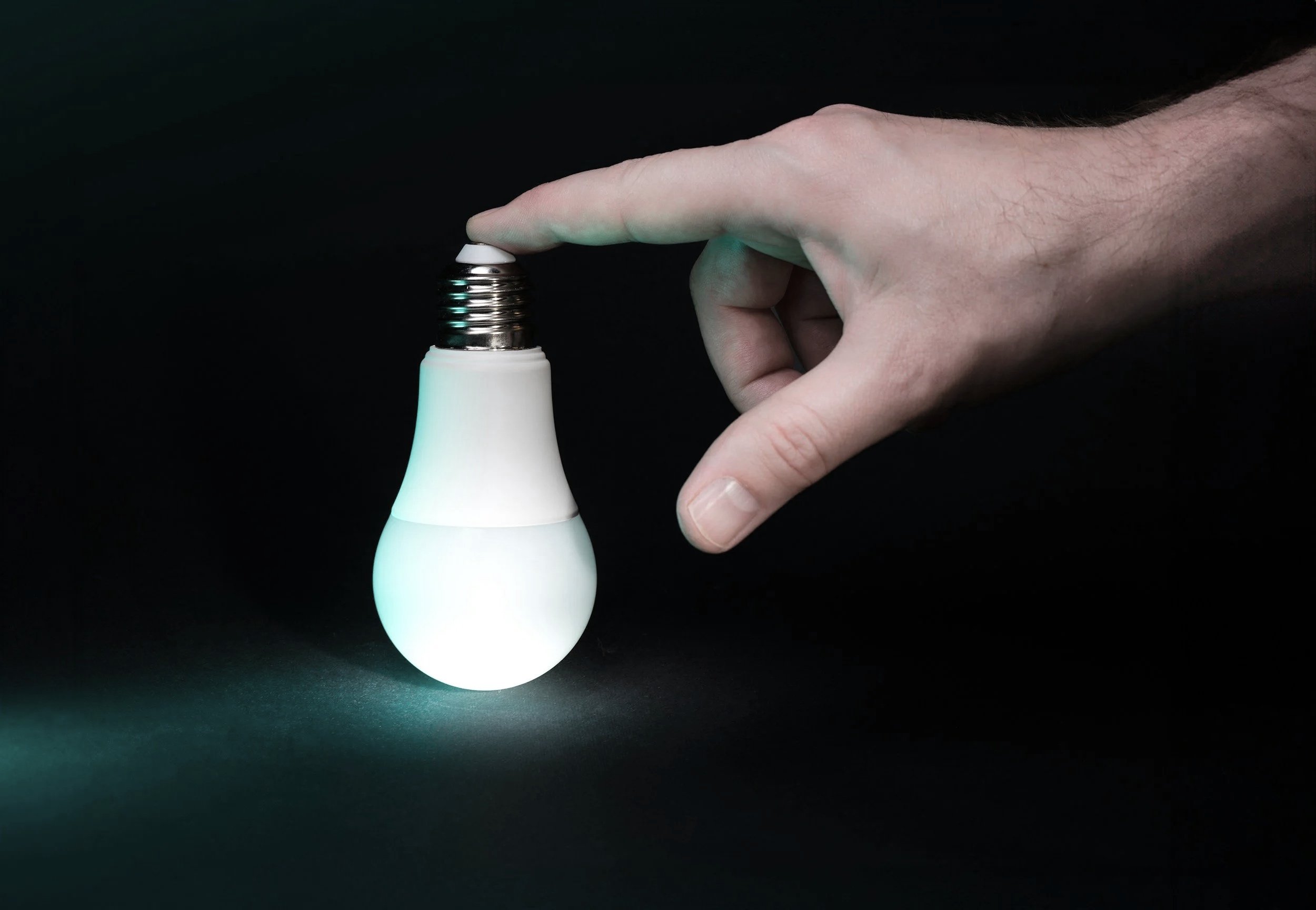 Hand, die ein LED-Glühbirne wie eine Glühbirne hält, die eine sanfte grüne Beleuchtung ausstrahlt, vor einem schwarzen Hintergrund.