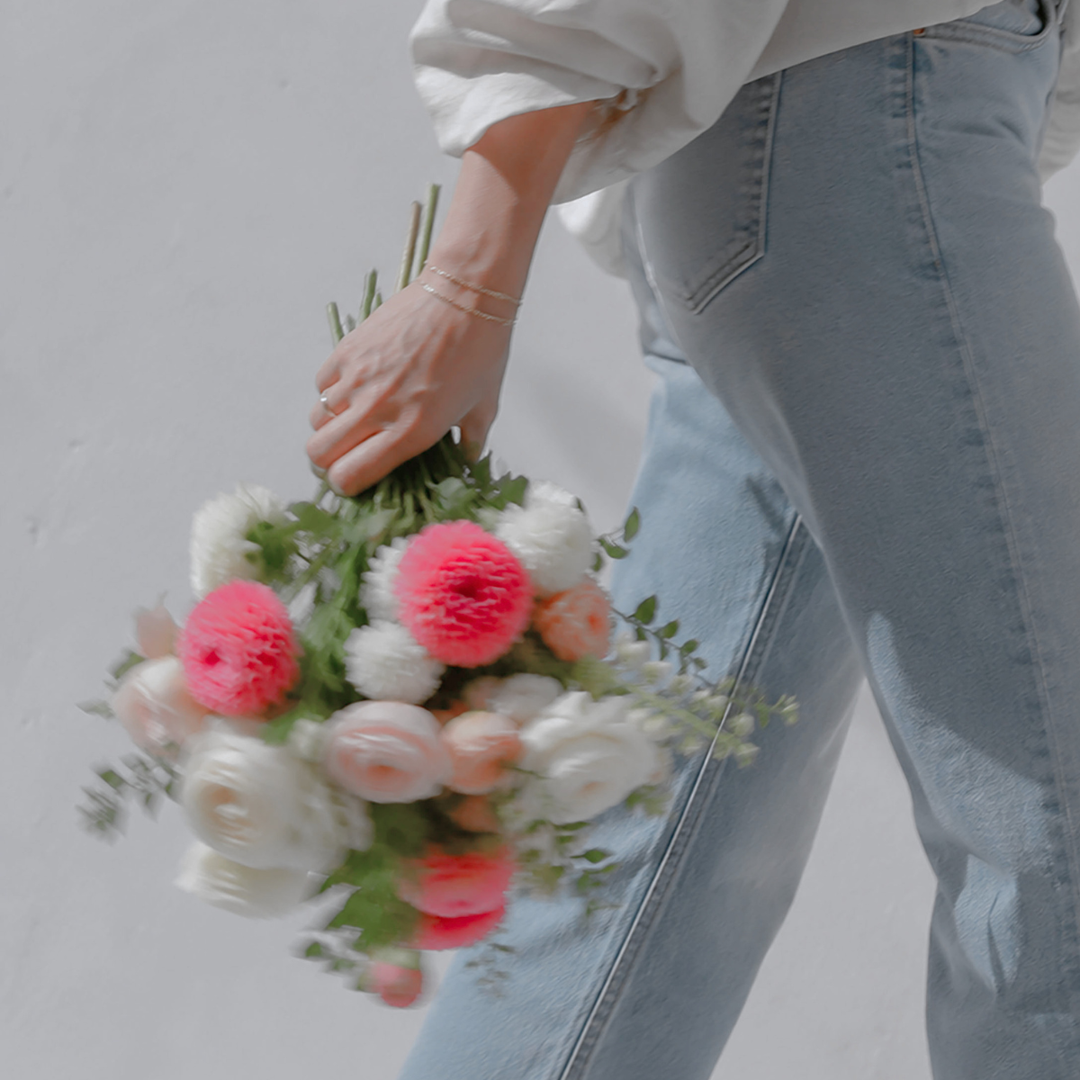 Person holding a bouquet of white, pink, and coral flowers while wearing light blue jeans and a white top.