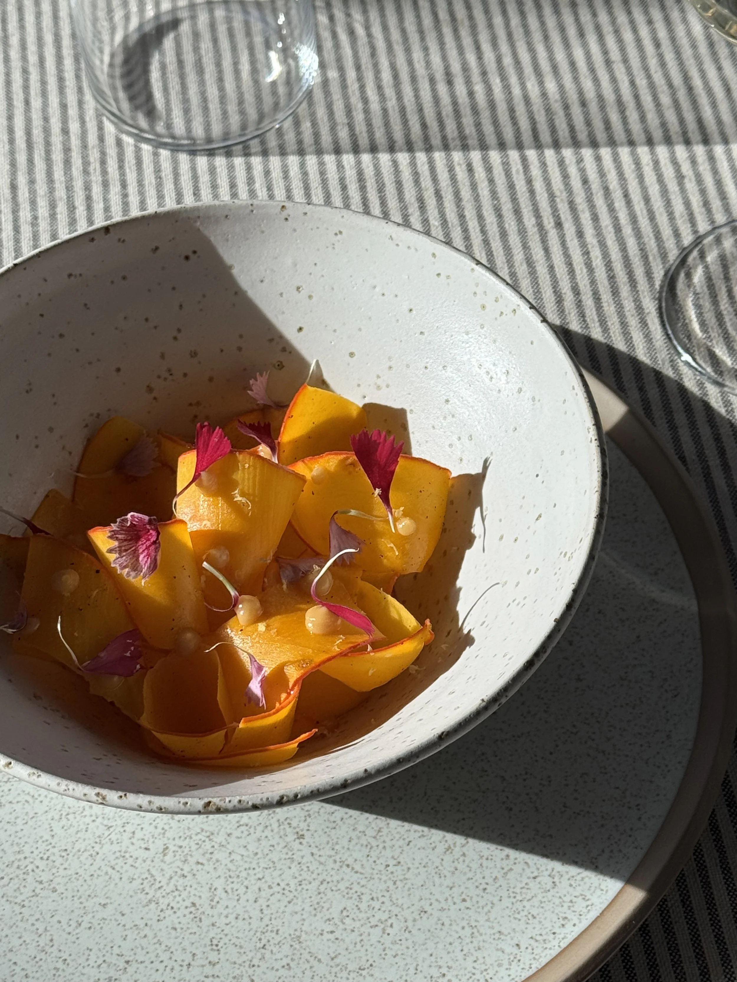 Une assiette de mangue fraîche garnie de fleurs comestibles roses, dans une cuisine ensoleillée.
