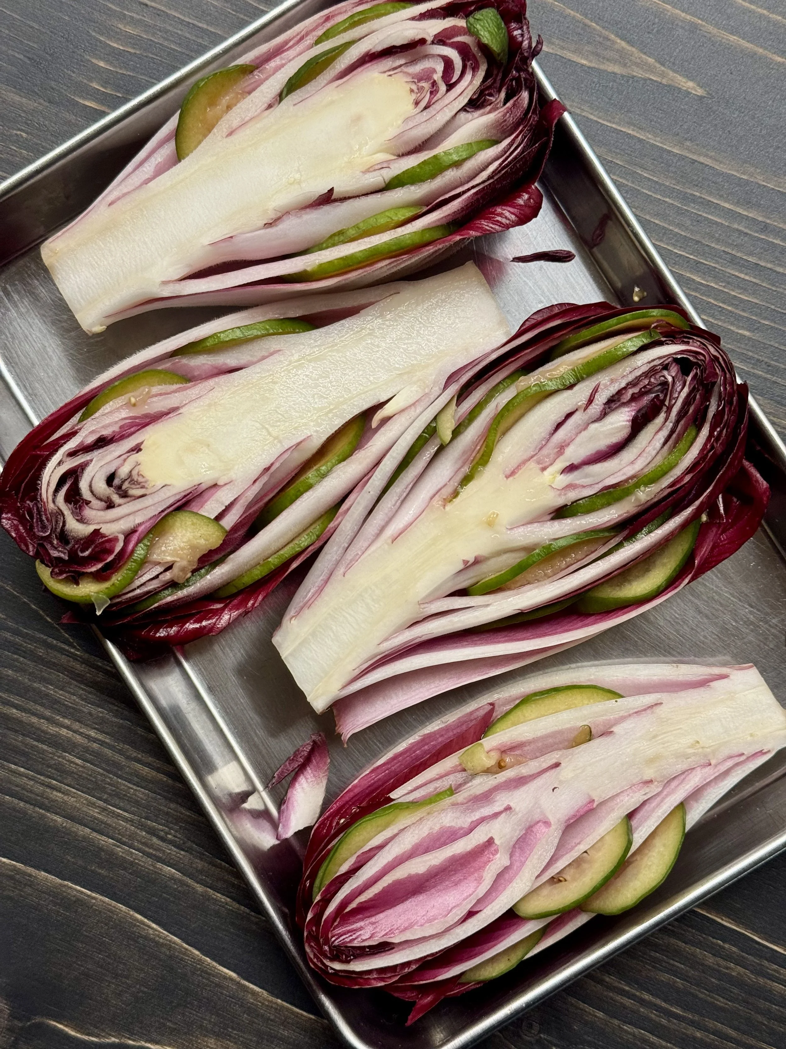 Fines tranches de radicchio, de endive et de concombre disposées dans une boîte en aluminium sur une table en bois.