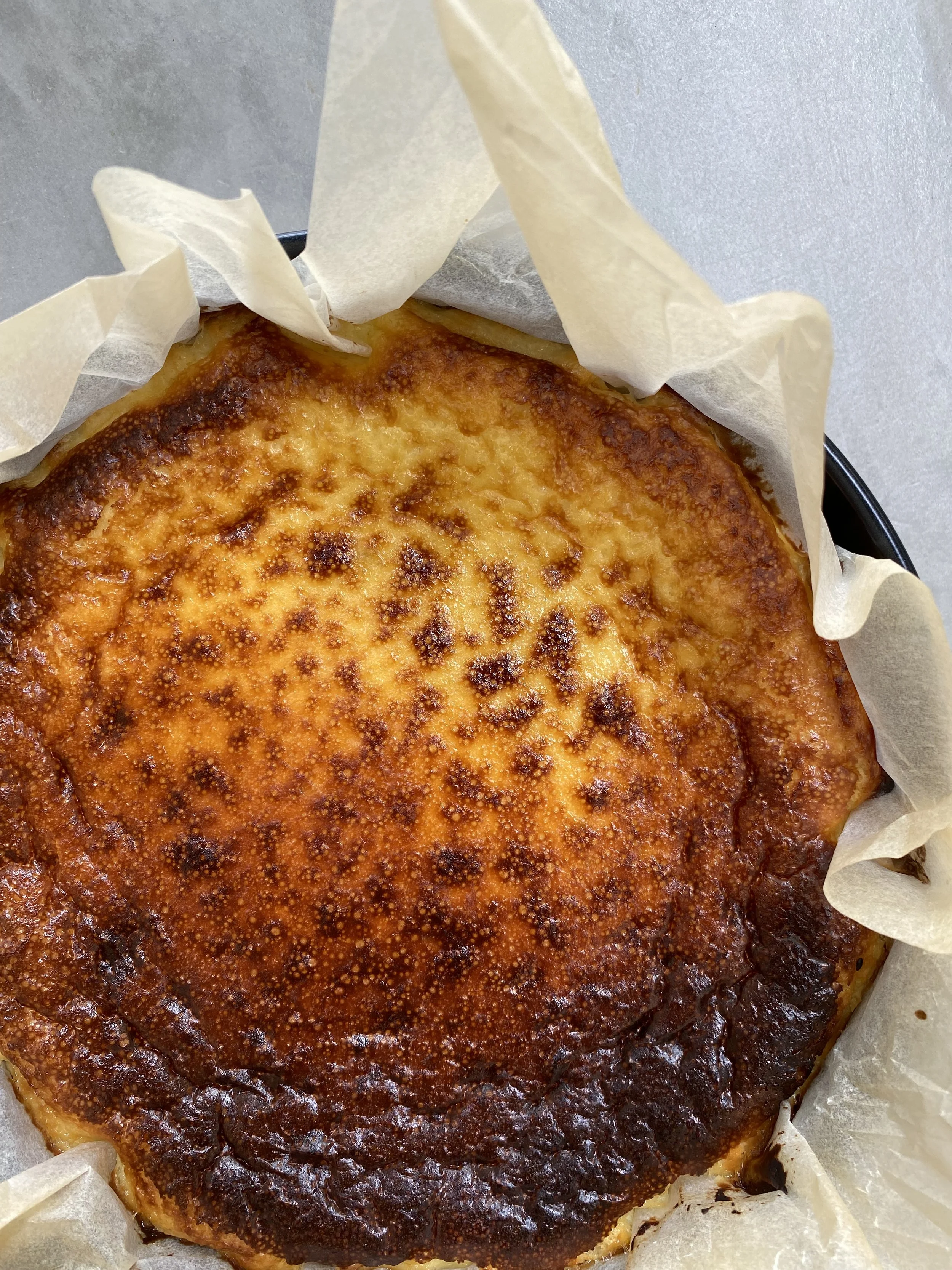 Gâteau titré cheesecake avec une croûte dorée, placé dans un papier de cuisson.