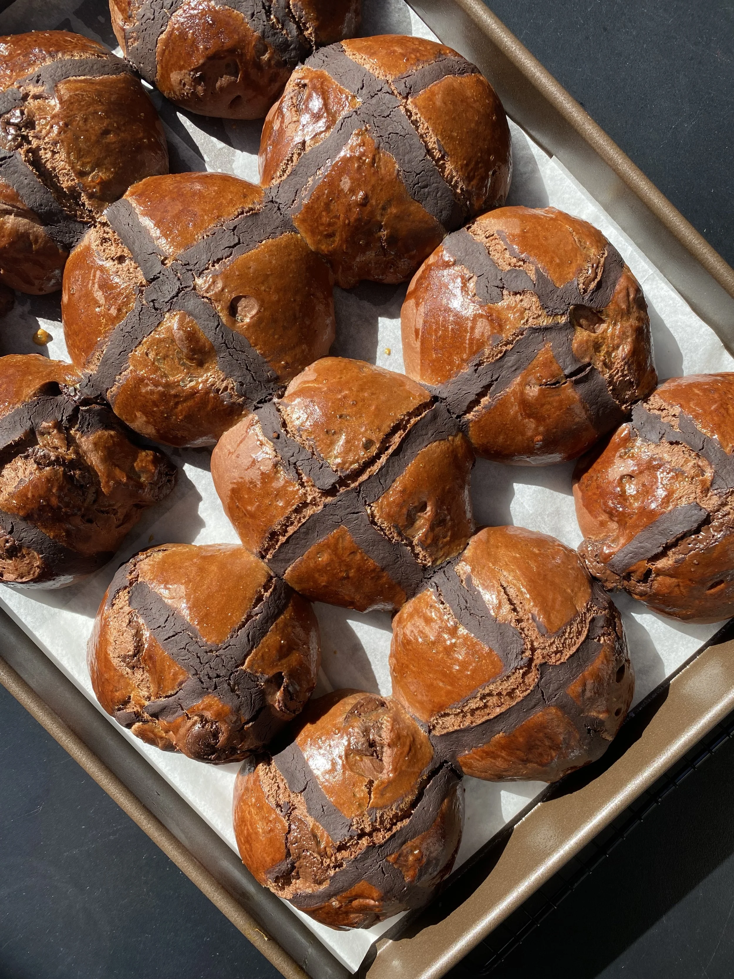 Gros plan de plusieurs brioches aux éclats de chocolat dorées, avec des encoches révélant du chocolat fondu, sur une plaque de cuisson