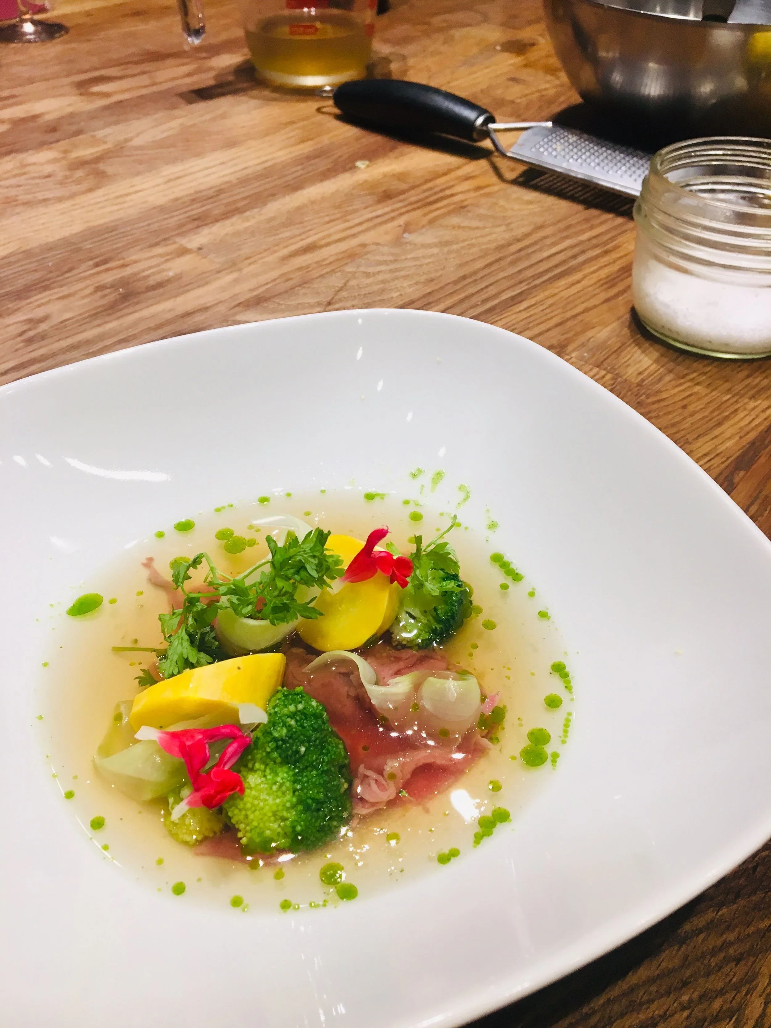 Assiette de soupe claire garnie de légumes verts, herbes, citron, et petits morceaux de viande, avec une cuillerée de sauce ou huile verte.