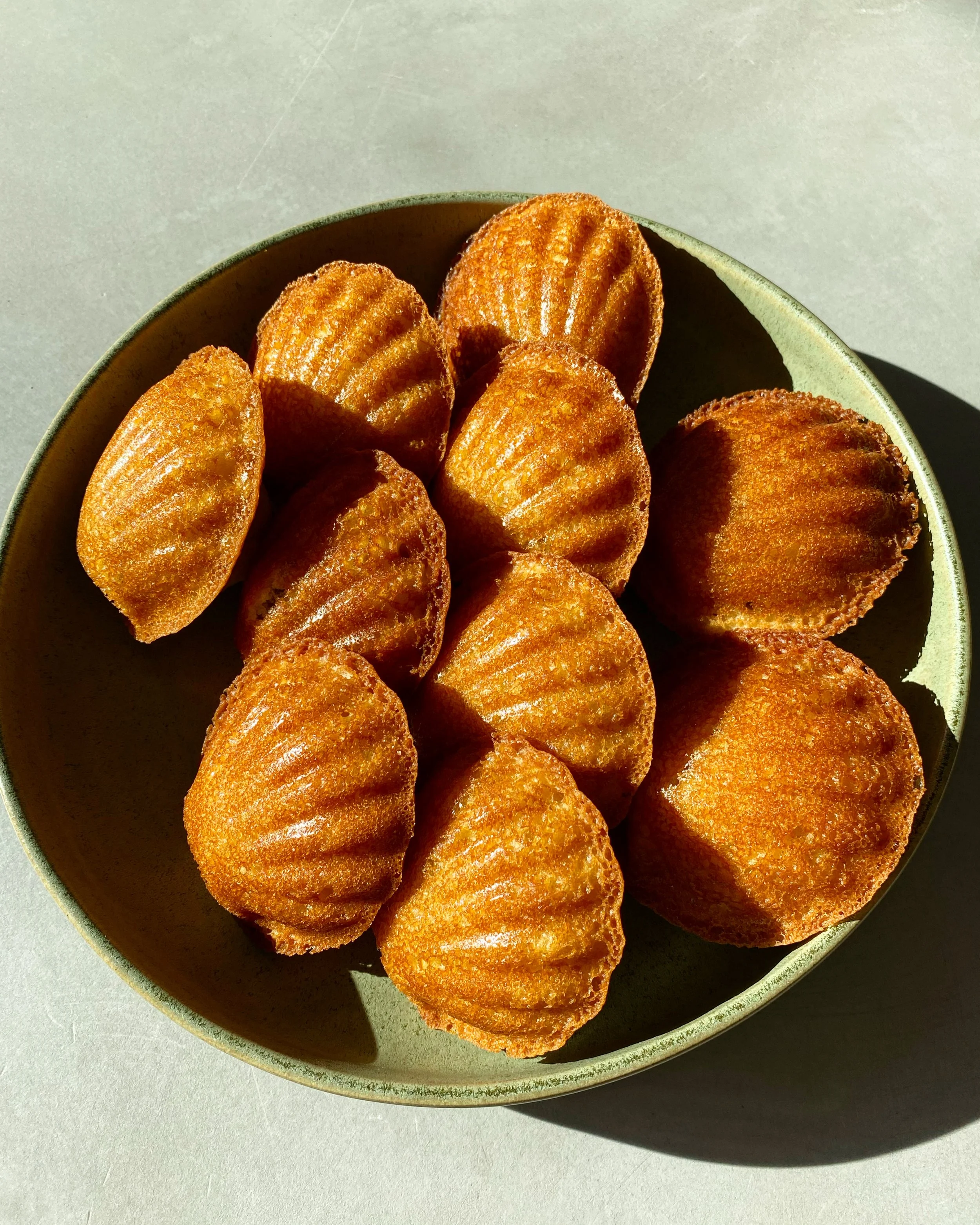 Gâteau madeleine dans un bol vert clair, vue de dessus, posé sur un fond gris.